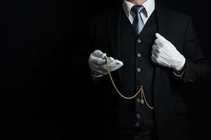 retrato de mayordomo con traje oscuro y guantes blancos con reloj de bolsillo dorado. estilo vintage y cortesía profesional. foto