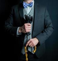 Portrait of Gentleman in Dark Suit Holding Leather Gloves and Umbrella on Black Background. Vintage Style and Retro Fashion. photo