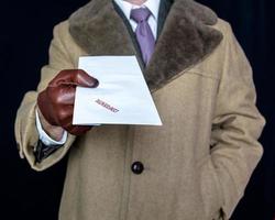 Portrait of Man in Fur Coat and Leather Gloves Handing Over  Confidential Envelope on Black Background. Film Noir Secret Agent Spy photo