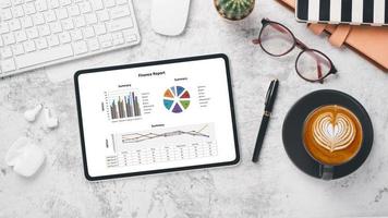 Tablet with charts and reports on office desk workplace. Top view flat lay photo