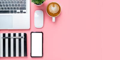 Office desk with laptop computer, Blank screen smart phone, cup of coffee, pen, Notebook on pink background, Top view with copy space, Mock up. photo