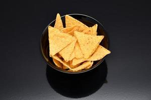 chips de tortilla amarilla en un tazón negro sobre fondo negro foto
