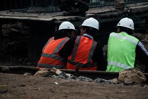 yakarta, indonesia en julio de 2022. tres trabajadores de la construcción descansan para relajarse después del trabajo sentándose en el borde del sitio de construcción foto