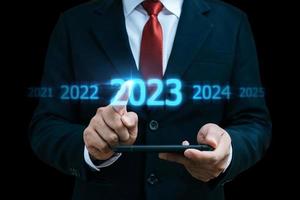 2023. mano de hombre de negocios tocando y señalando el año 2023 con pantalla virtual sobre fondo oscuro, meta, cambio de 2022 a 2023, estrategia, inversión, planificación empresarial, concepto de feliz año nuevo foto