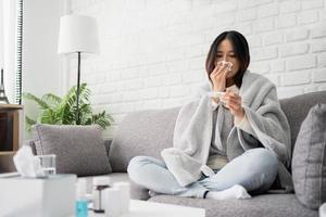 una joven asiática enferma está comprobando la temperatura corporal en casa. sentía frío y tenía fiebre, así que se cubrió con una manta. foto