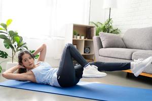 Portrait of Asian woman in sportswear exercising on yoga mat in living room at home. Fitness and healthy lifestyle. photo