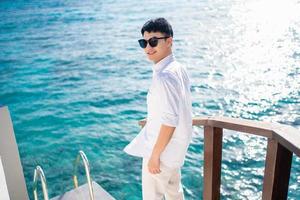 Happy asian man in sunglasses standing at sea on vacation photo