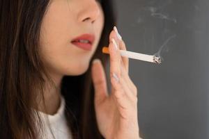 Close up hand holding cigarette, Asian woman smoking outdoors. photo