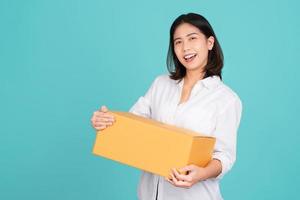 Happy Asian woman smiling in white casual dress standing smiling and looking at camera. She is holding package parcel box isolated on light green background.