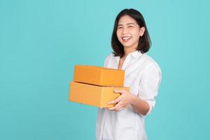 Happy Asian woman smiling wearing white shirt and holding package parcel box isolated on white background, Delivery courier and shipping service concept photo