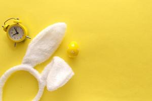 Decorated Easter eggs and bunny ears on color yellow background, top view photo