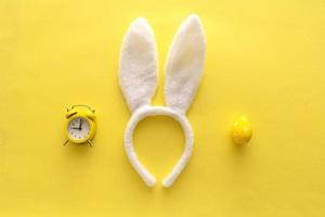 Decorated Easter eggs and bunny ears on color yellow background, top view photo