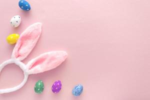 Decorated Easter eggs and bunny ears on color pink background, top view photo