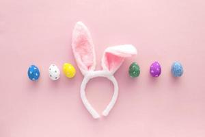 Decorated Easter eggs and bunny ears on color pink background, top view photo