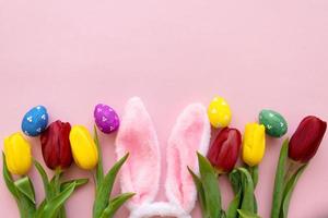 beautiful tulips, decorated Easter eggs and bunny ears on color pink background, top view photo