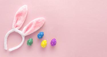 huevos de pascua decorados y orejas de conejo sobre fondo de color rosa, vista superior foto