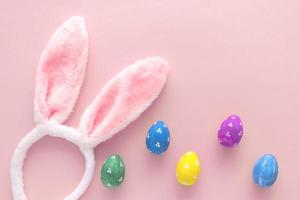 Decorated Easter eggs and bunny ears on color pink background, top view photo