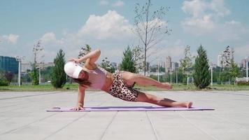 senhora atlética em roupas esportivas está bombeando os abdominais. mulher em forma está fazendo exercícios abdominais no parque da cidade. estilo de vida saudável, conceito de treino ao ar livre. câmera lenta. video