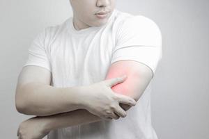 dolor muscular, dolor en el brazo, sensación de ardor, músculos débiles, síndrome de oficina, desgarro muscular causado por el ejercicio, zona roja inflamada. hombre con dolor de brazo en un fondo gris. concepto de salud foto