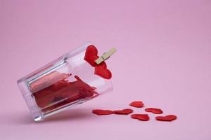 An overturned glass glass on a pink background is filled with red hearts photo