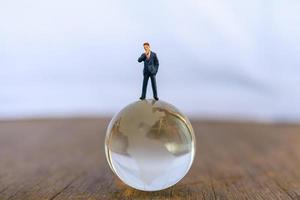 concepto global y de negocios. figura de personas en miniatura de empresario de pie en el modelo de bola de cristal claro mundo. foto