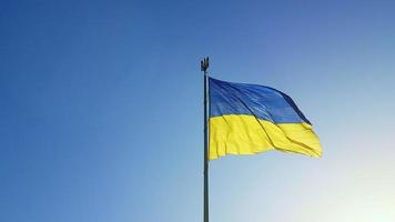 The Ukrainian flag of blue and yellow national colors on the flagpole flutters in the wind against the blue sky and the morning rising sun. The official state symbol of Ukrainians. Patriotism. photo