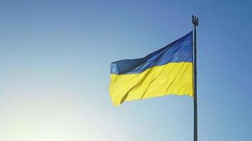 The Ukrainian flag of blue and yellow national colors on the flagpole flutters in the wind against the blue sky and the morning rising sun. The official state symbol of Ukrainians. Patriotism. photo