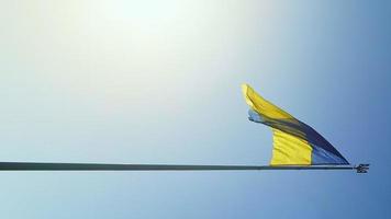 la bandera ucraniana de colores nacionales azul y amarillo en el asta de la bandera ondea en el viento contra el cielo azul y el sol naciente de la mañana. el símbolo oficial del estado de los ucranianos. vídeos verticales. foto