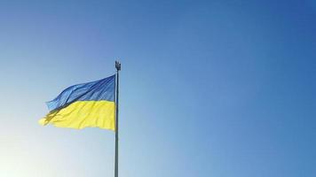 The Ukrainian flag of blue and yellow national colors on the flagpole flutters in the wind against the blue sky and the morning rising sun. The official state symbol of Ukrainians. Patriotism. photo