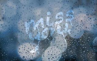 Miss you on wet window glass. Blue blurred grainy background with city light and bokeh. Glass with raindrops and stains from finger drawing. Abstract aesthetic backdrop. Romantic emotion , lonely photo