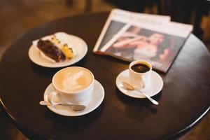 close up a mug of fragrant cappuccino and a sweet dessert and a magazine on the table photo