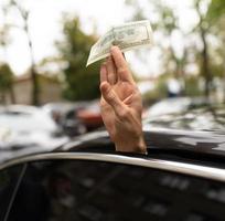 una mano extendida desde el auto sostiene un billete de 100 dólares. foto