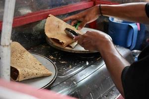 un joven vendedor está haciendo crepes de bocadillos en una calle cerca de un parque temático foto