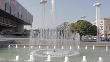 fuentes en jarkov. fuente alta pública en el centro de la ciudad, rociando agua en un parque soleado, la gente camina y se relaja en el parque. ucrania, kharkiv - 17 de julio de 2021. video