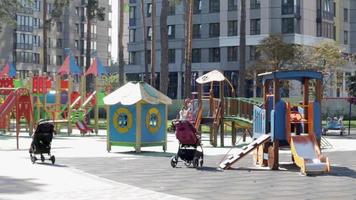 colorido parque infantil moderno en el patio del parque con gente relajante y niños juguetones. parque infantil en un parque público rodeado de árboles verdes y casas nuevas. ucrania, Kyiv - 29 de junio de 2021. video