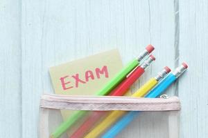 exam word in a sticky note and pencils on color background photo