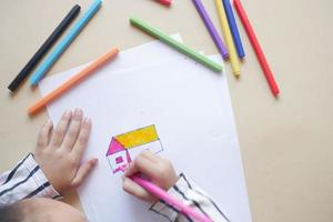top view of child girl drawing a house with color pencils on paper photo