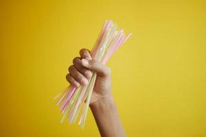 C holding many plastic straws against yellow photo