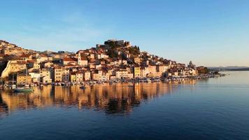 Aerial drone view of Sibenik town in Croatia during beautiful sunset colors, with a boat passing on the sea. Vacations and holidays on the seacoast. The Cathedral of St James in Sibenik Unesco. video