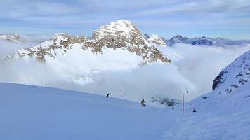 gente esquiando. vista invernal de las montañas con nubes debajo de la estación de esquí. actividades y deportes de invierno. estilo de vida aventurero. estación de esquí kanin, sella nevea en la frontera de eslovenia e italia.