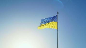 de ukrainska flagga av blå och gul nationell färger på de flaggstång fladdrar i de vind mot de blå himmel och de morgon- stigande Sol. de officiell stat symbol av ukrainare. patriotism. video