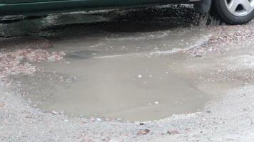 baches llenos de agua en una carretera asfaltada con coches que pasan. clima lluvioso. el coche conduce a través de charcos en carreteras asfaltadas rotas después de la lluvia durante el día. gotas de lluvia y coches en la carretera. video