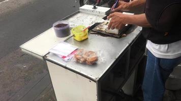 fazendo lanches tradicionais pukis. pukis é feito de massa de farinha misturada com açúcar e polvilhada com chocolate e depois moldada com ferro fundido video