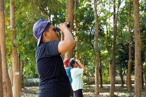 los niños asiáticos usan binoculares para observar las aves en un bosque comunitario. el concepto de aprendizaje de fuentes de aprendizaje fuera de la escuela. Centrarse en el primer hijo. foto