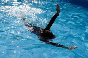 una chica con traje de baño negro nadaba en la piscina. en el concepto de pasatiempos, verano, actividades de ocio, natación infantil. enfoque suave y selectivo. foto