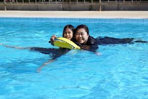 An Asian girl floats in a tube with her mother, both smiling happily in the swimming pool. Soft and selective focus. photo