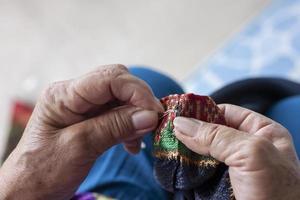 Old hand women sew hooks for attaching clothes. photo