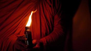handhållen skott, natt scen, stänga upp hand av munk innehav en liten flaska belyst förbi en fotogen lampa
