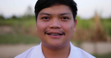 Portrait Close up of an Asian young happy farmer man looking at camera and smiling with a farmland background. Agriculture farming concept. Slow motion. video