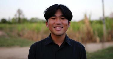 Portrait of an Asian young happy farmer man looking at camera and smiling with a farmland background. Agriculture farming concept. Slow motion. video